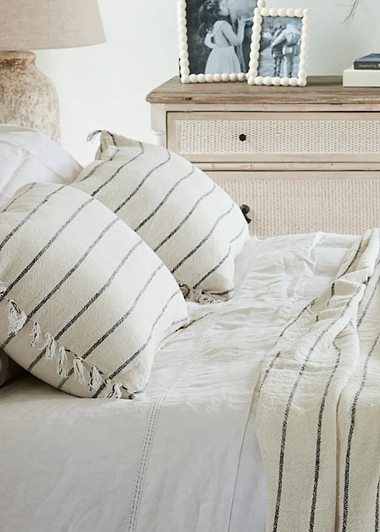 Neatly made bed with striped bedding and pillows, dresser in the background.