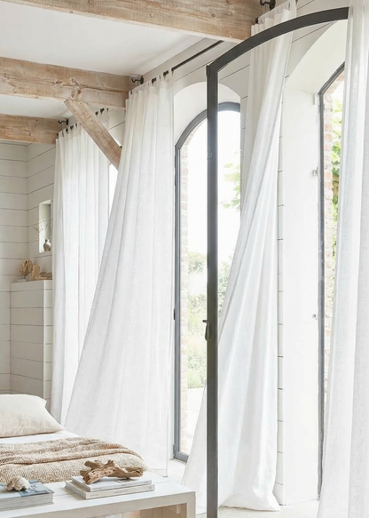 Modern bedroom with large windows, white curtains, and a wooden bed.