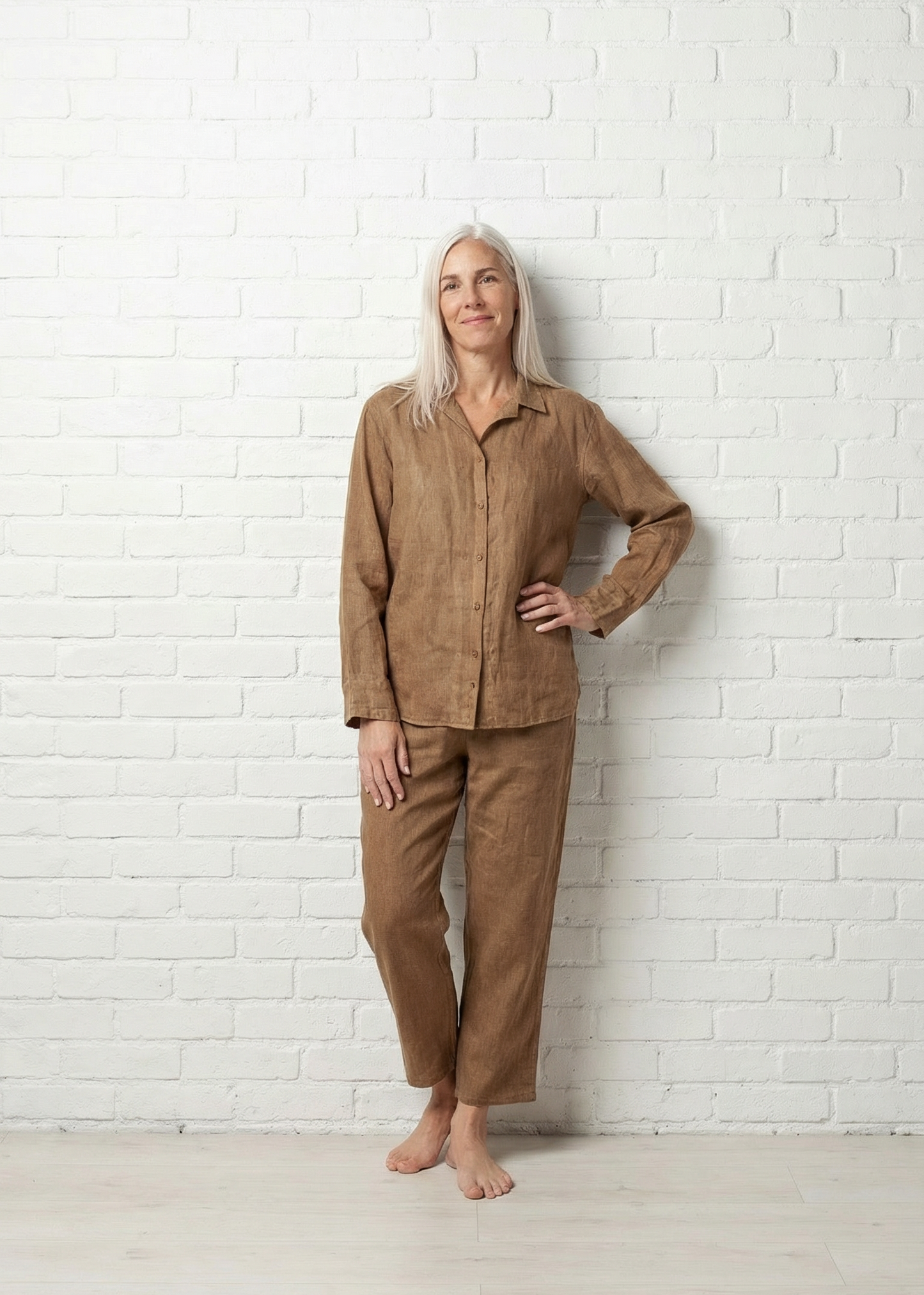 Woman wearing a brown linen outfit against a white brick wall.