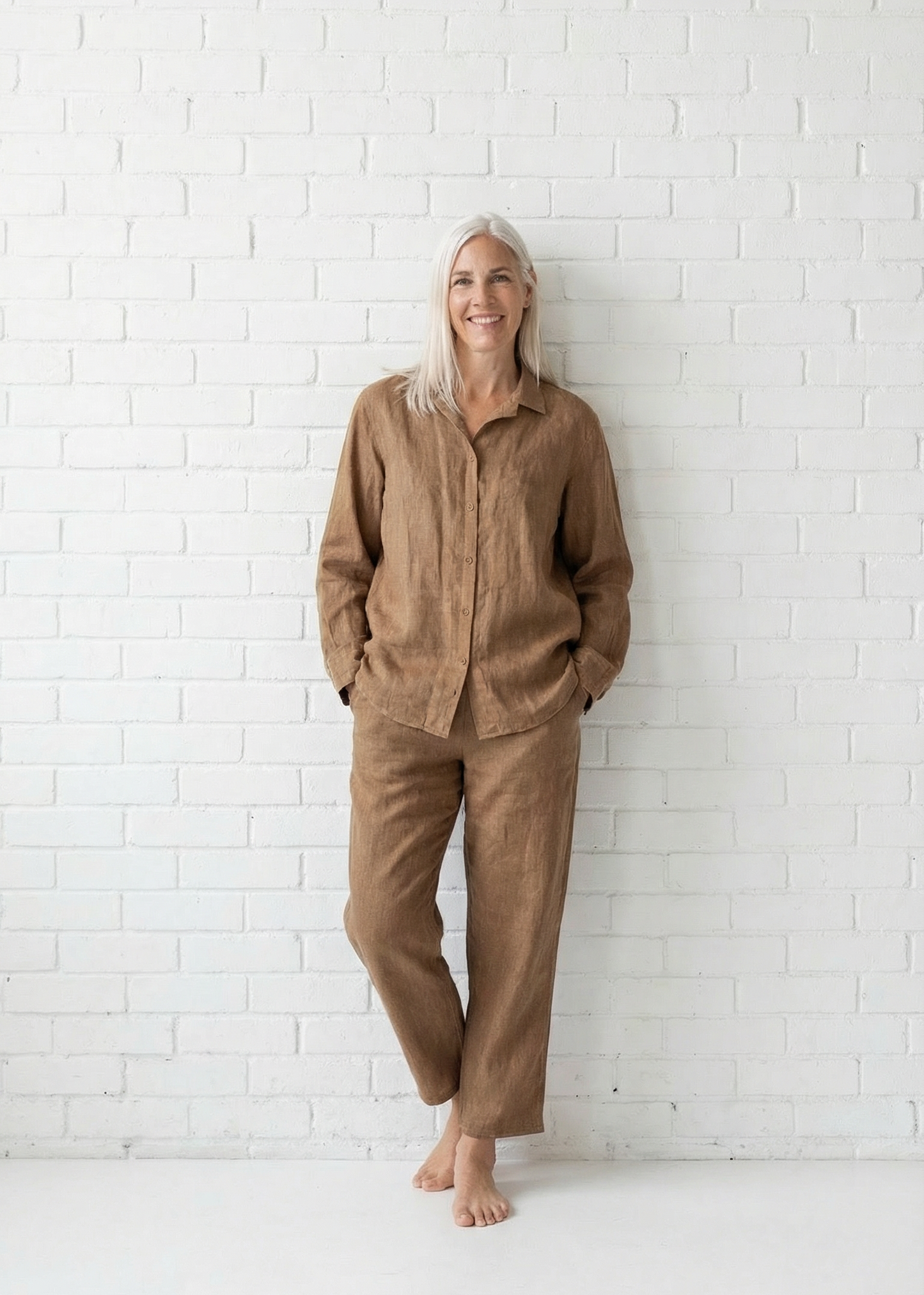 Woman wearing a brown outfit standing against a white brick wall.