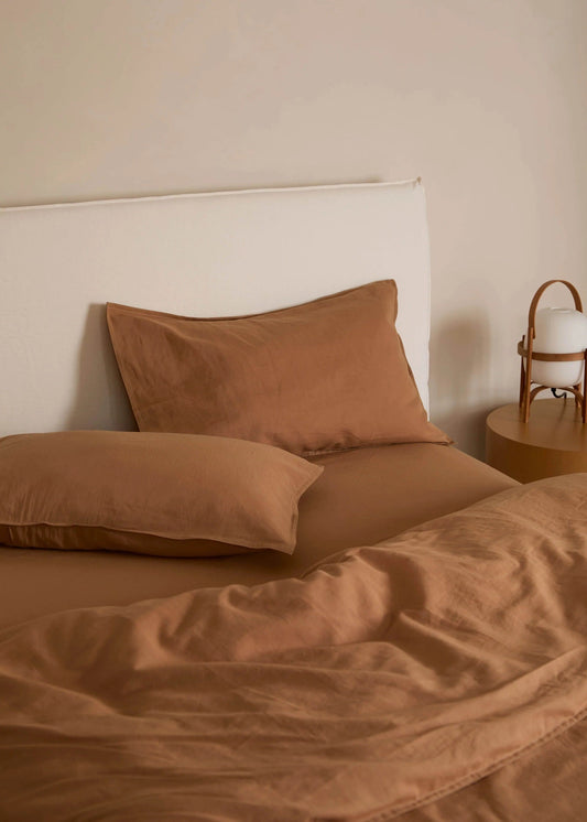 Brown bedding set on a bed with a neutral headboard and side table.