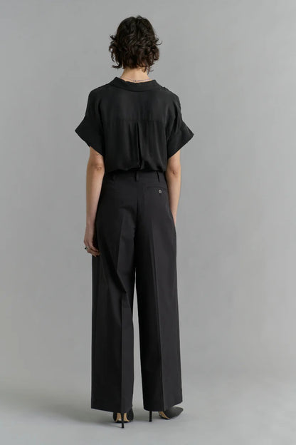 Person wearing a black outfit with wide-leg pants on a gray background