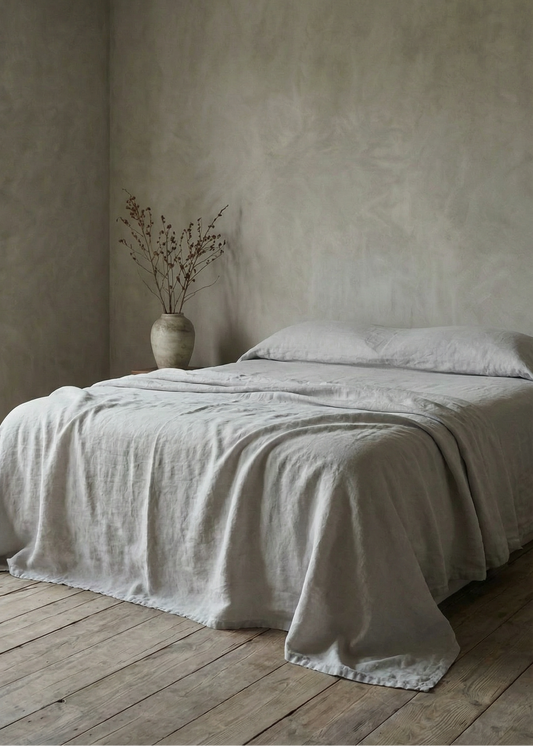 Bedroom with a bed covered in a beige blanket, wooden floor, and neutral walls.