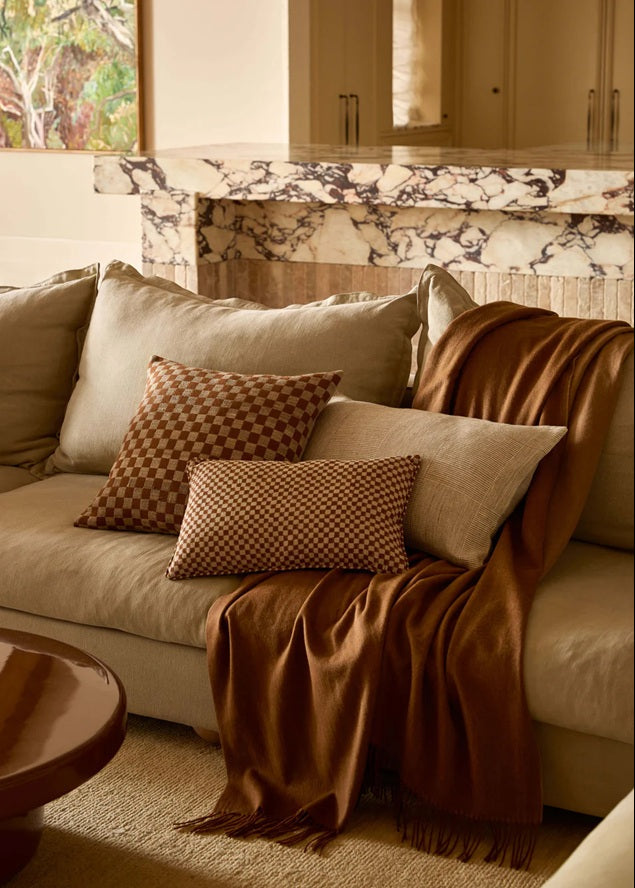 Cozy living room with a beige sofa, brown throw blanket, and patterned pillows.