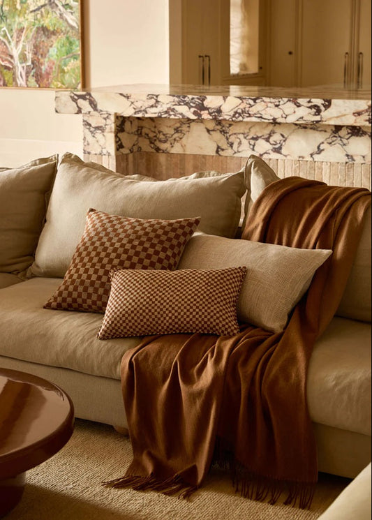 Cozy living room with a beige sofa, brown throw blanket, and patterned pillows.