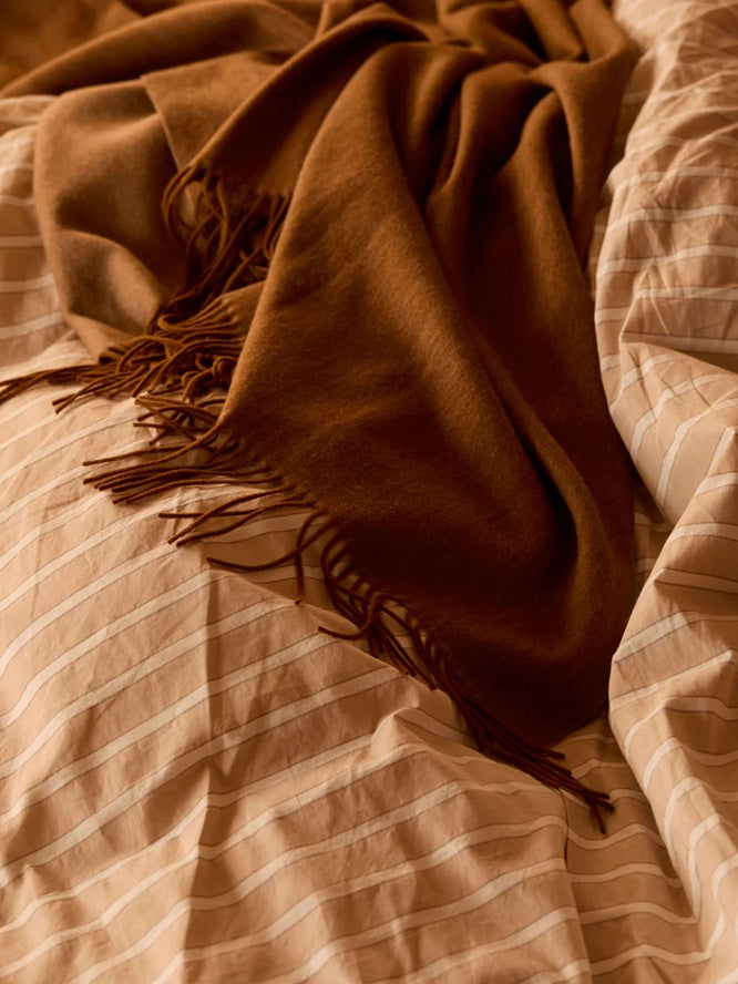 Brown blanket with fringes draped over a striped fabric surface