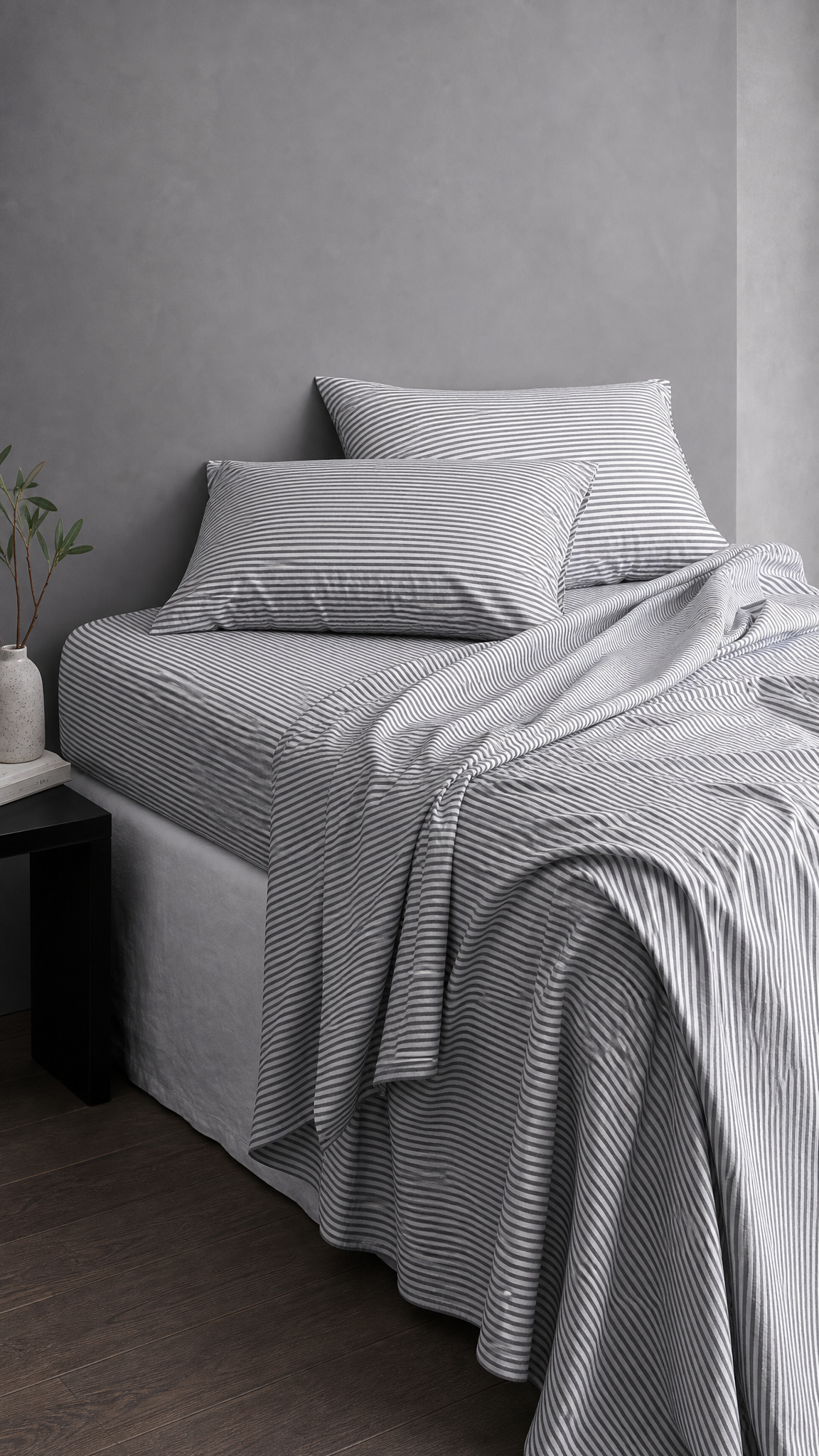 Striped bedding set with matching pillowcases and a draped throw blanket on a bed in a minimalist bedroom setting.