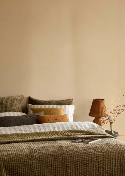 Cozy bedroom with a bed covered in brown and beige bedding, a lamp, and a window.