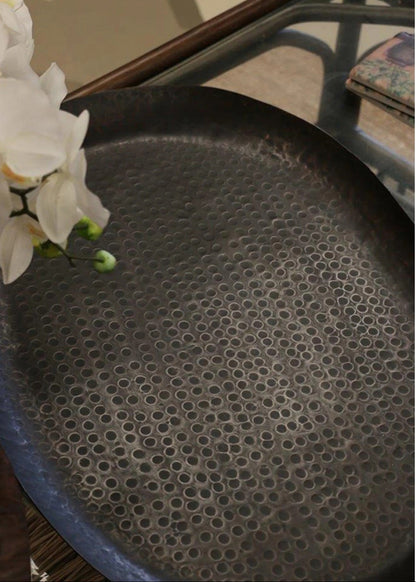 Round black textured tray on a surface with a white flower and book in the background