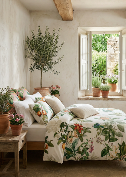 Cozy bedroom with floral bedding, plants, and a window view of greenery.