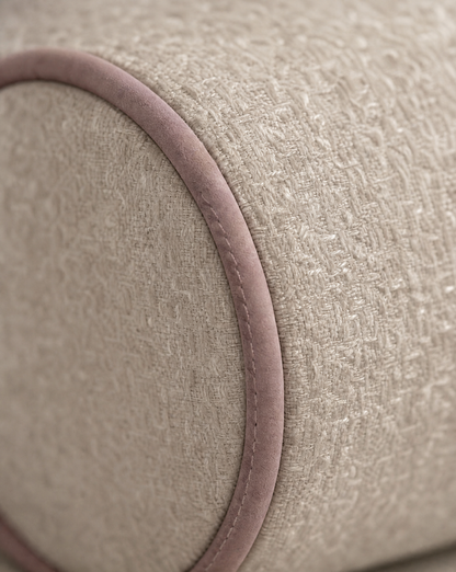 Close-up of a textured beige fabric cylindrical cushion with a contrasting dusty rose velvet trim.