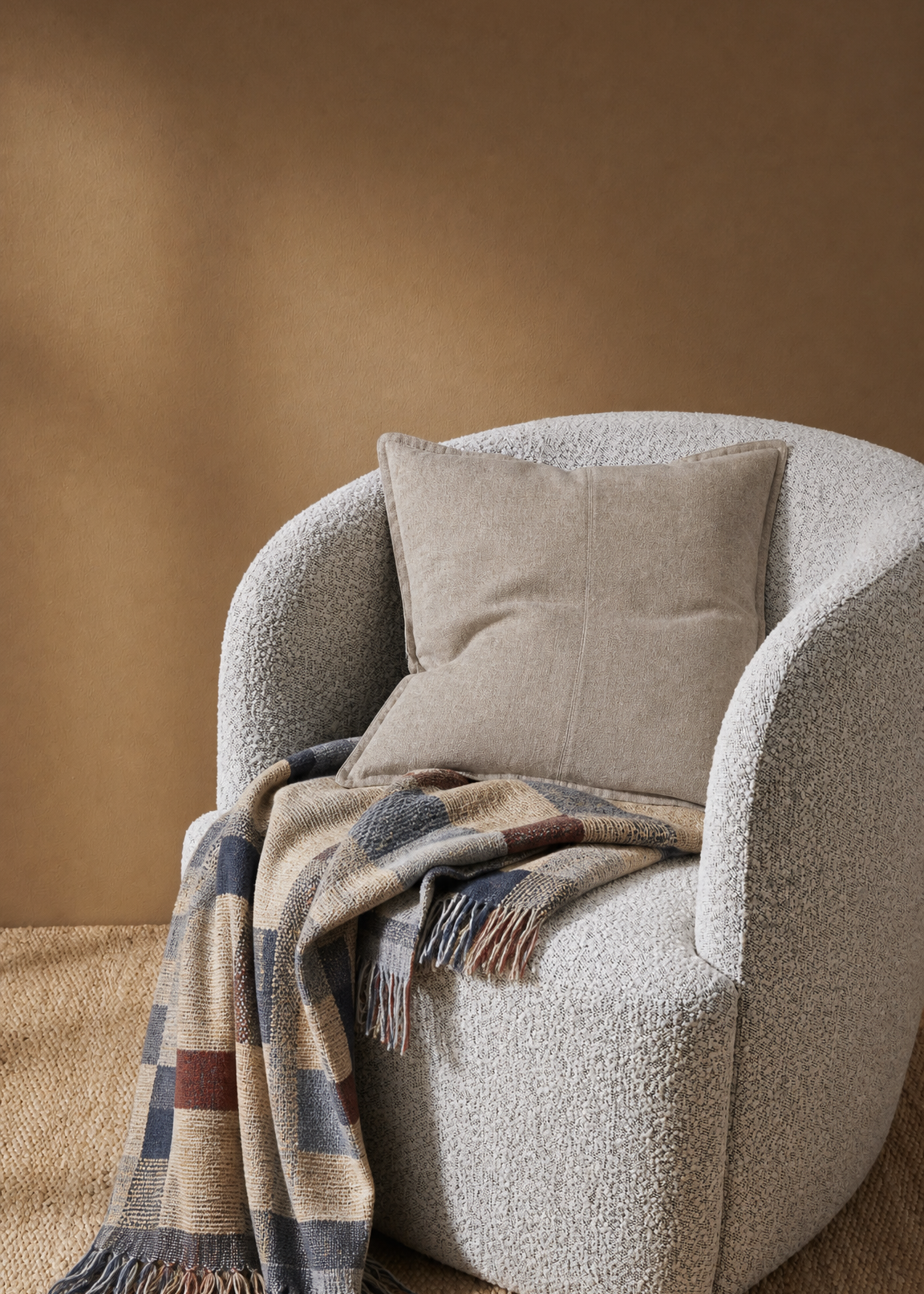 Gray armchair with a plaid blanket and beige pillow against a brown wall.