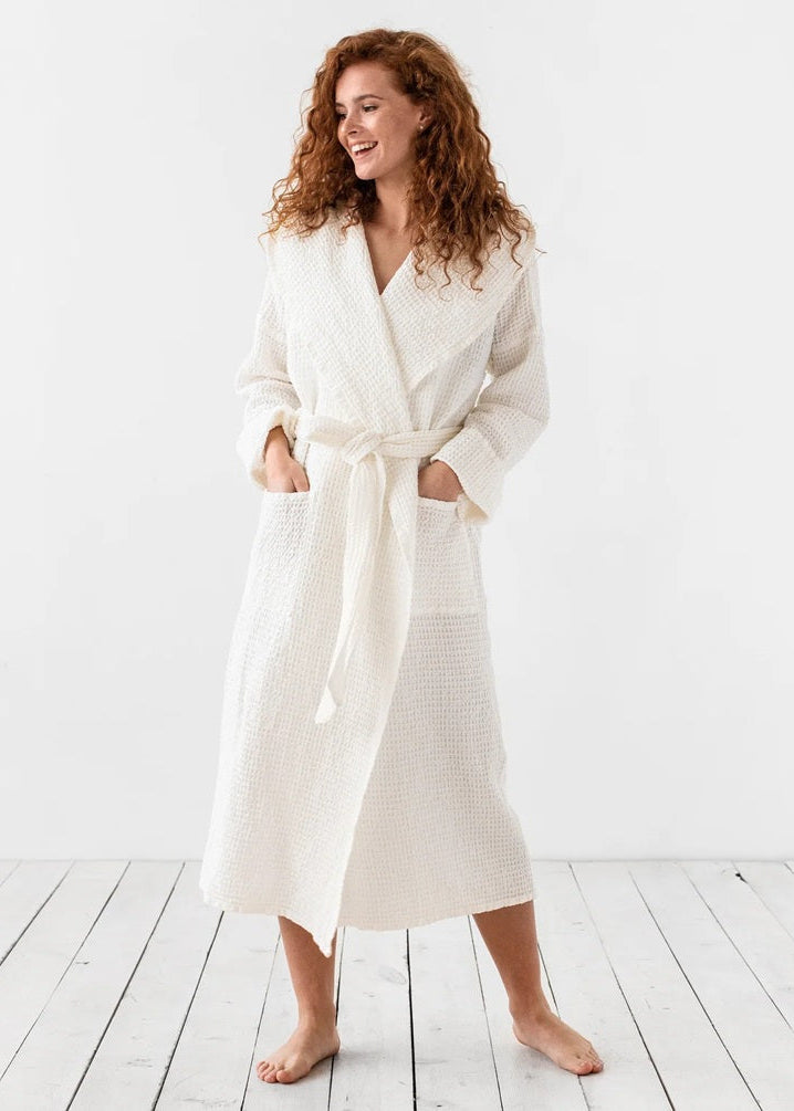 Woman wearing a white robe standing on a wooden floor with a white background