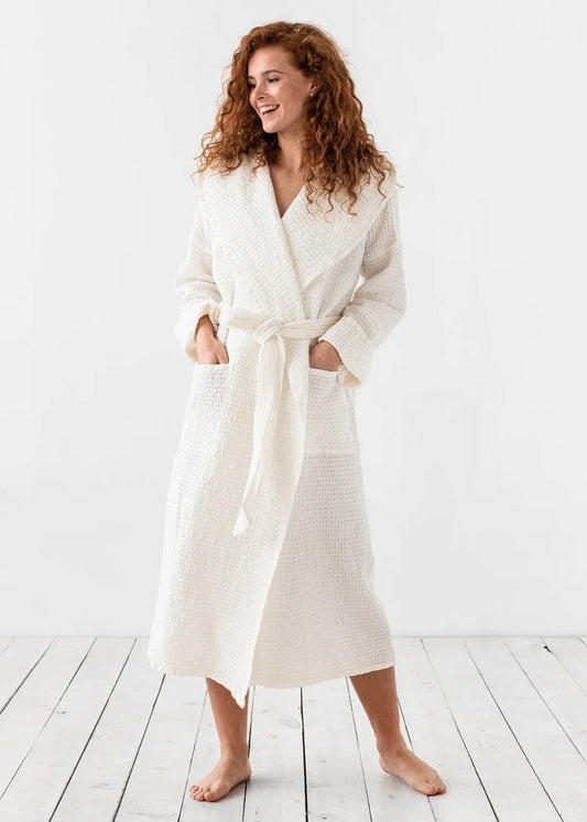 Woman wearing a white robe standing on a wooden floor with a white background