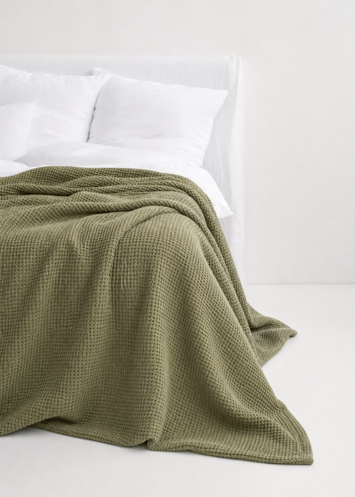 Green blanket on a bed with white pillows against a white background
