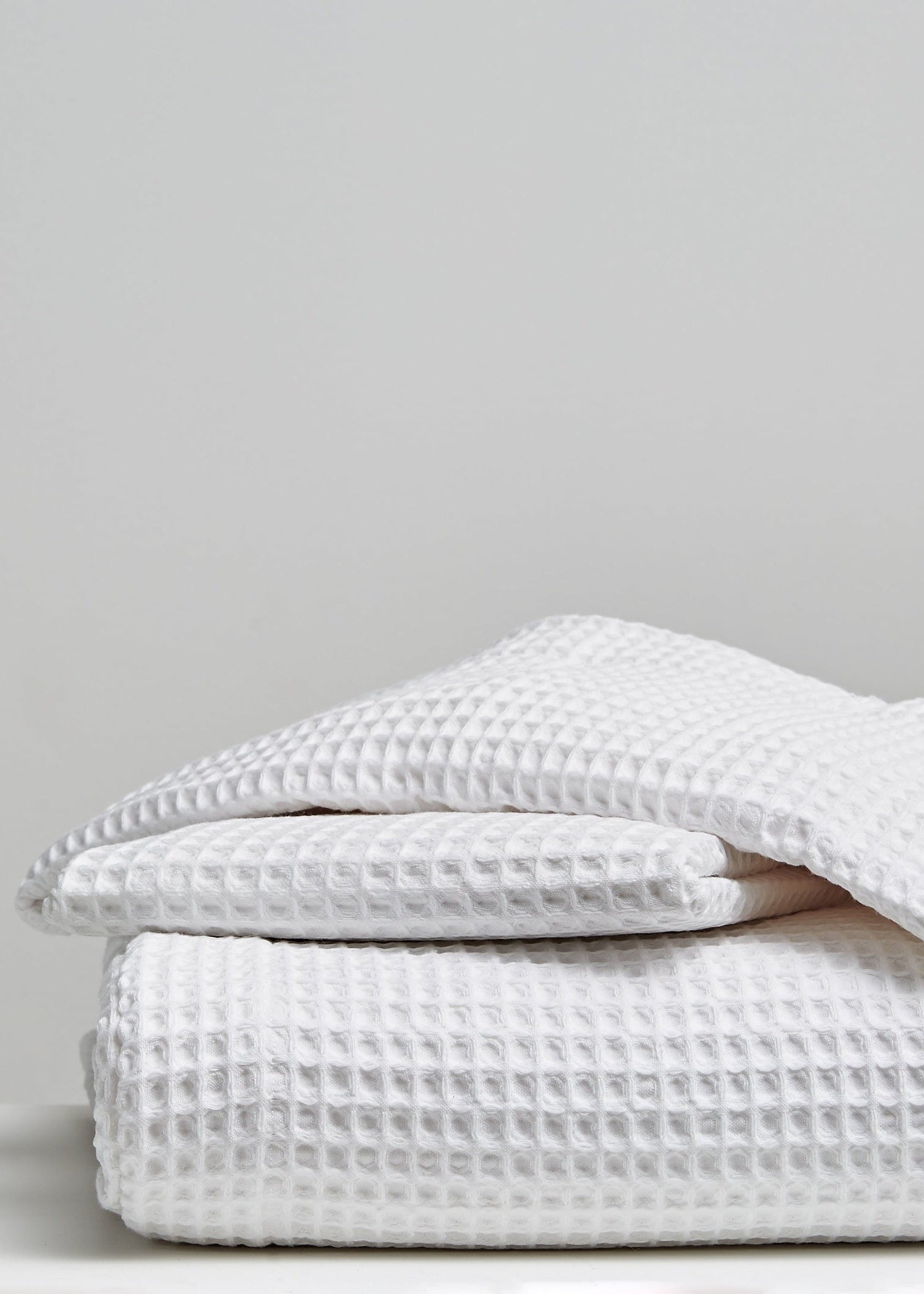 A stack of folded white waffle-weave textiles, likely towels or blankets, photographed on a light gray background.