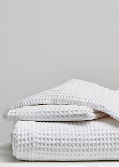 A stack of folded white waffle-weave textiles, likely towels or blankets, photographed on a light gray background.