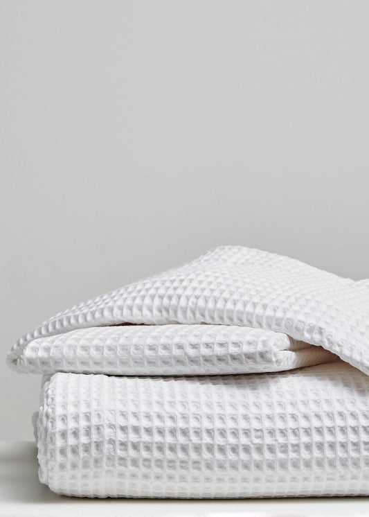 A stack of folded white waffle-weave textiles, likely towels or blankets, photographed on a light gray background.