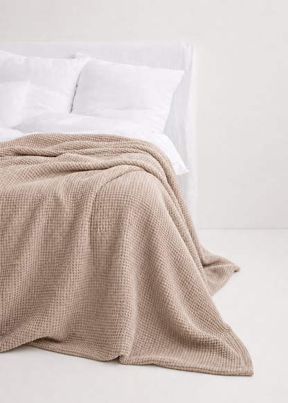 Beige blanket on a bed with white pillows against a light background