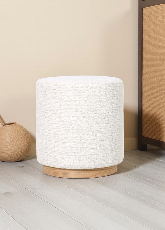 White textured cylindrical lamp on a wooden base next to a woven basket and wooden cabinet.