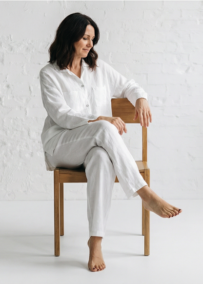 Woman sitting on a wooden chair wearing a white outfit against a white background