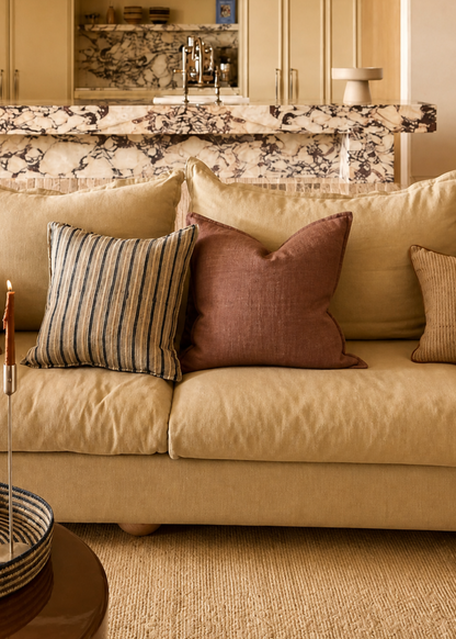 Living room with beige sofa, decorative pillows, and a kitchen in the background.