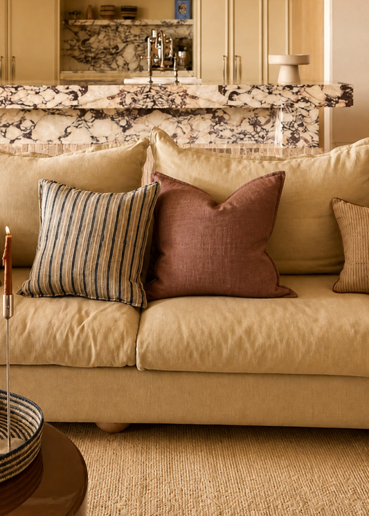 Living room with beige sofa, decorative pillows, and a kitchen in the background.