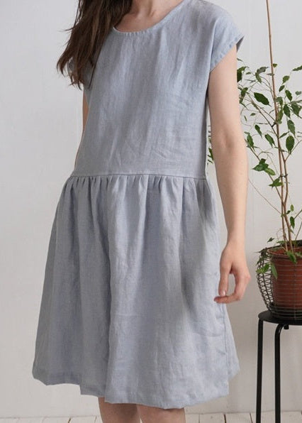 Woman wearing a light blue dress standing next to a potted plant indoors.