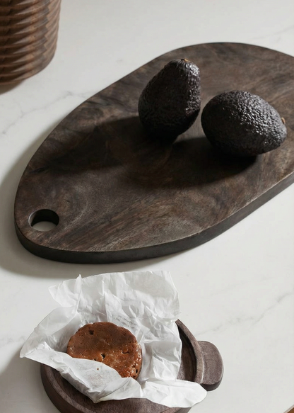 Wooden cutting board with avocados and a piece of paper on a white surface