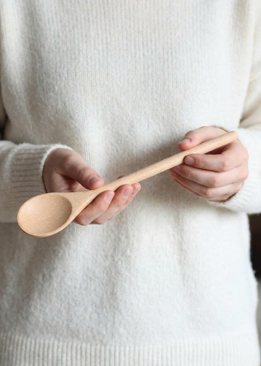 Person holding a wooden spoon against a neutral background