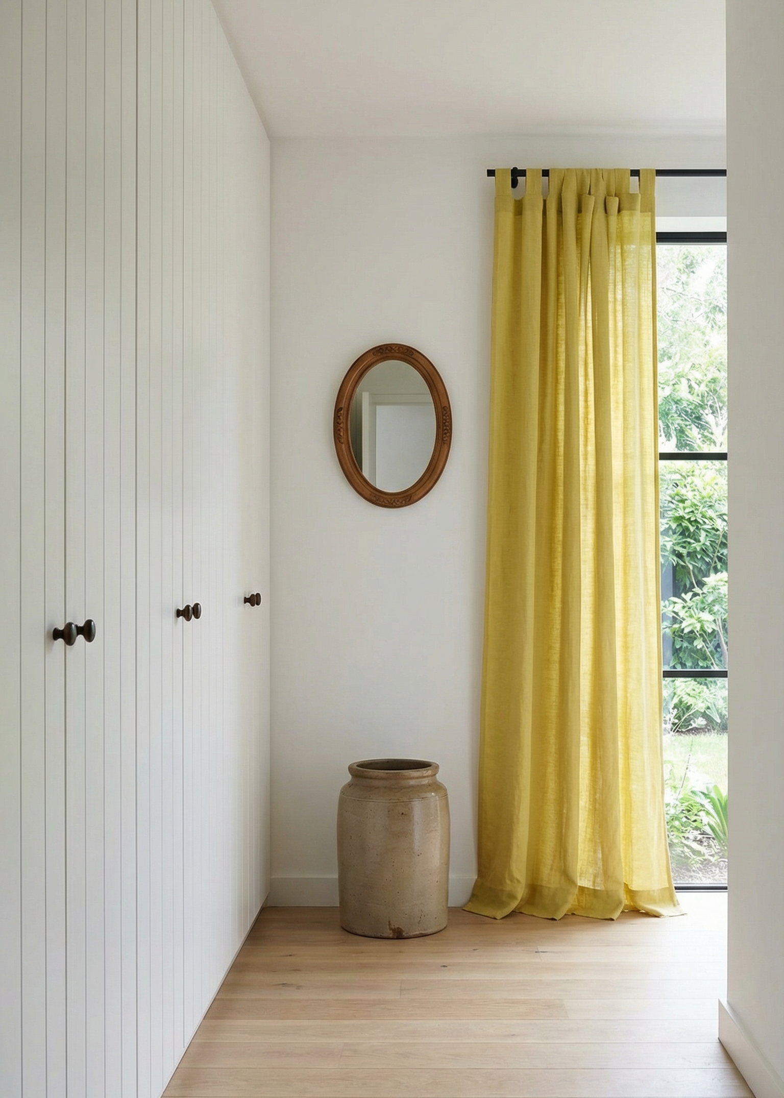 Narrow hallway with yellow curtains, a mirror, and a vase.