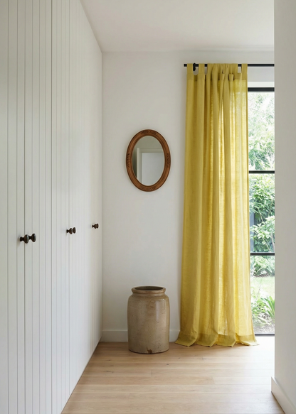 Narrow hallway with yellow curtains, a mirror, and a vase.