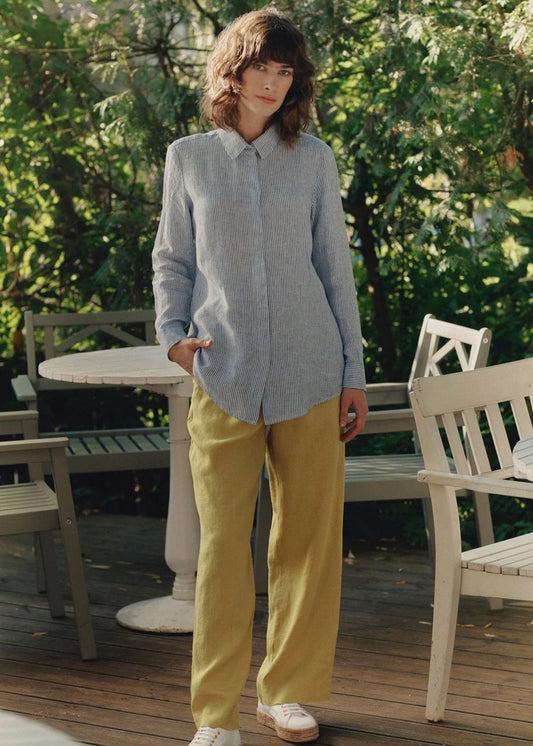 Person wearing a light blue shirt and yellow pants standing on a wooden deck with greenery in the background
