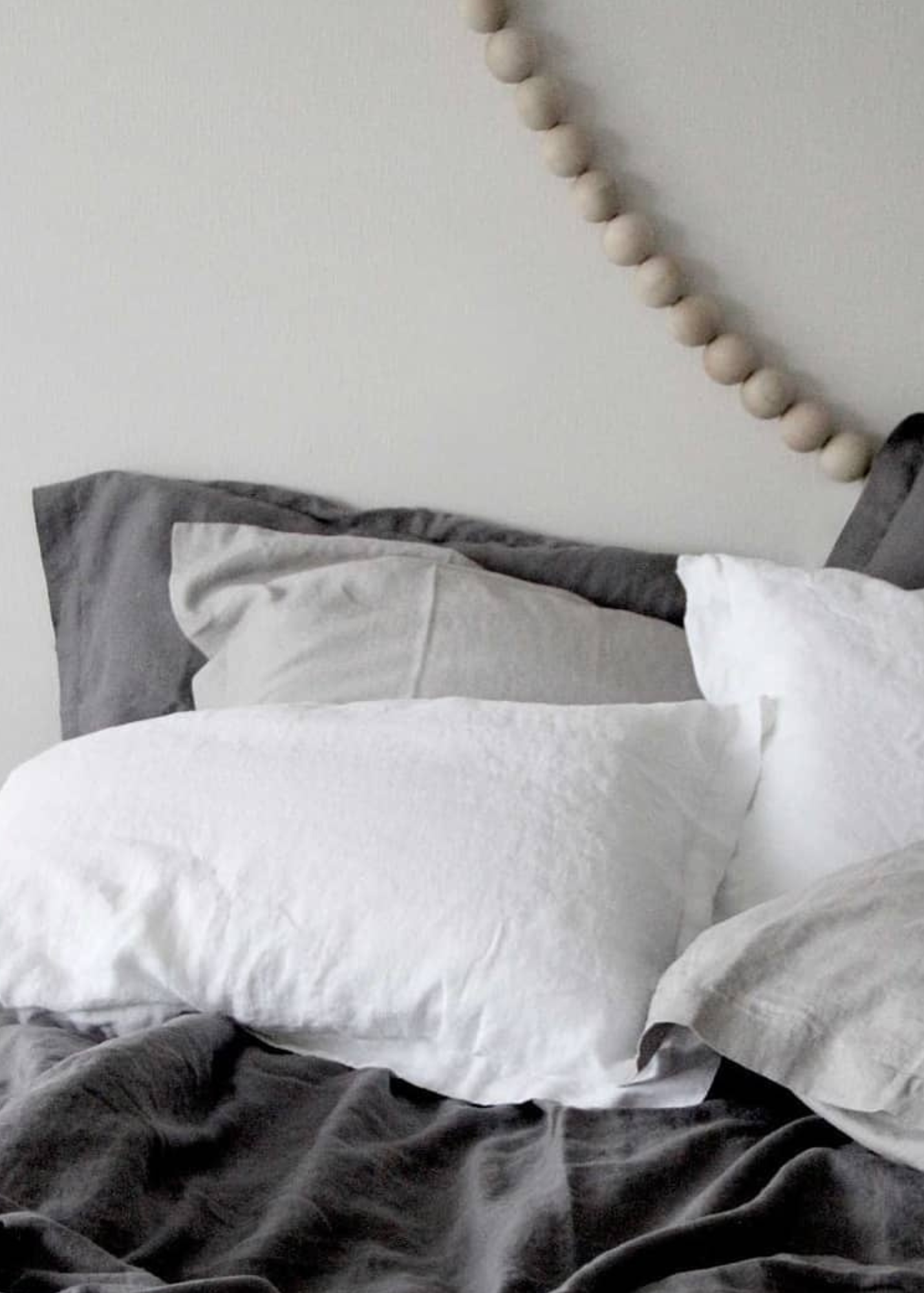 White linen pillowcases on a bed with gray bedding, in a room with a decorative wall hanging.
