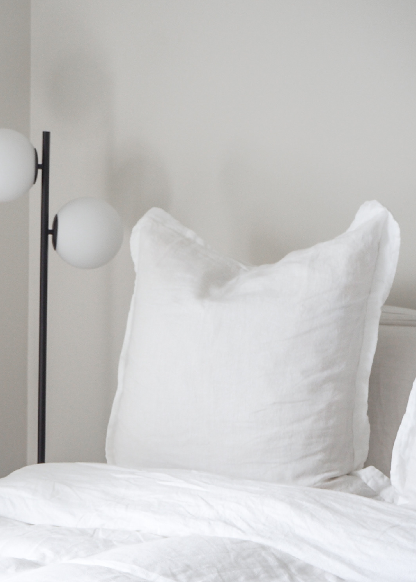 A pure white linen euro pillowcase displayed on a bed, with a modern floor lamp beside it.