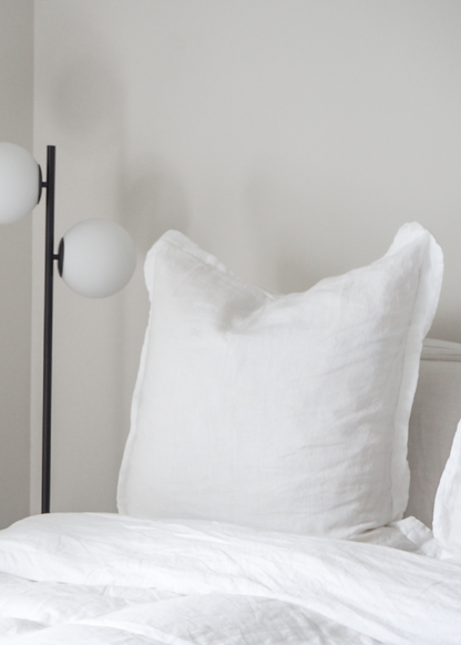A pure white linen euro pillowcase displayed on a bed, with a modern floor lamp beside it.