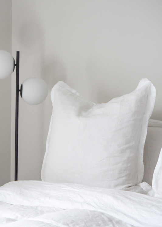 A pure white linen euro pillowcase displayed on a bed, with a modern floor lamp beside it.