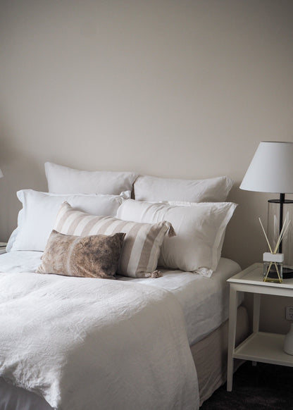 A white linen duvet cover displayed on a bed with accompanying pillows, bedstand, and lamp.